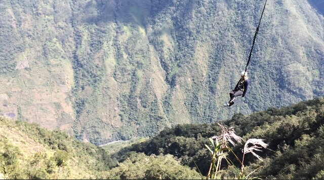 woman on harness and line hanging above valley in mountains