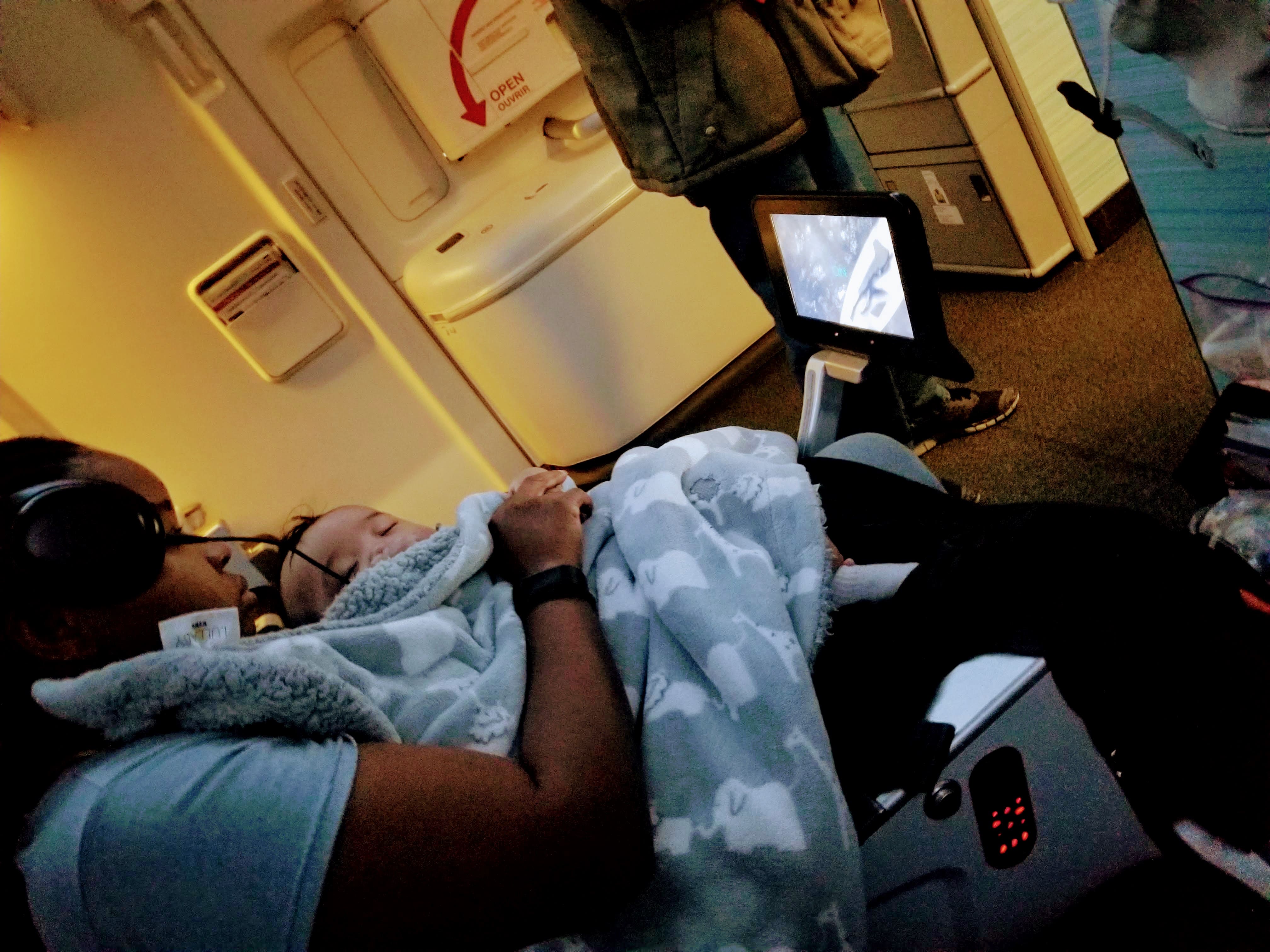 woman with baby on plane seat watching TV